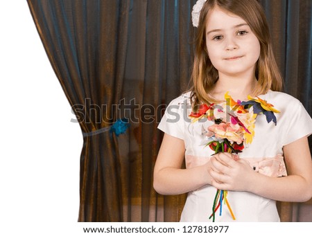 Beautiful little girl posing with a handful of colourful artificial flowers against a curtain drawn aside on the left to reveal blank white copyspace