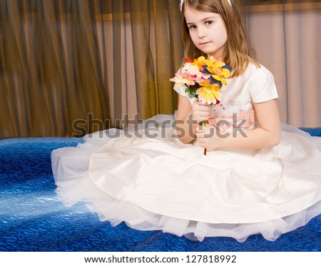 Beautiful little girl posing sitting on the floor on a blue carpet in a tutu with the filmy gauze skirt spread out around her while she holds a bouquet of flowers in her hands