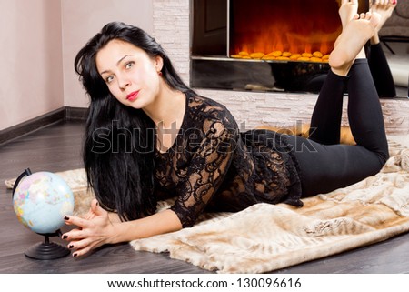 Attractive barefoot young woman lying in front of the fire with a globe in front of her dreaming of her summer vacation and travels