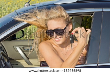 Windblown woman sitting in a car with her head out of the window holding a key between her fingers