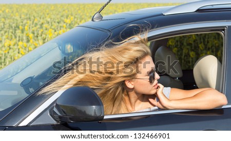 Beautiful female driver in car looking back with her head out of the window and her blonde hair blowing in the wind