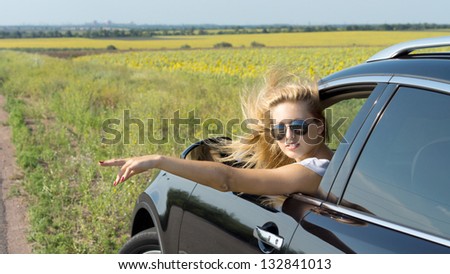 Pretty blande female passenger leaning out of a car window giving a hand signal to turn onto the road