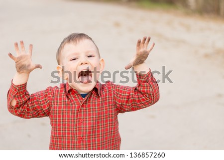 Cute little boy trying to scare the viewer with his hands raised and mouth open yelling, high angle portrait outdoors