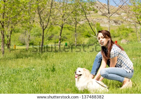 Profile portrait of an attractive young woman and her adorable little fluffy dog posing together in long green grass in a rural landscape