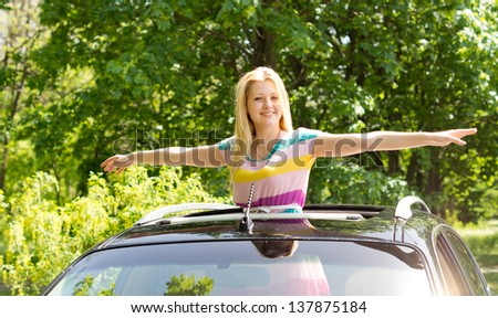 Image of a gorgeous young female spreading her hands like a bird outside a moving car.