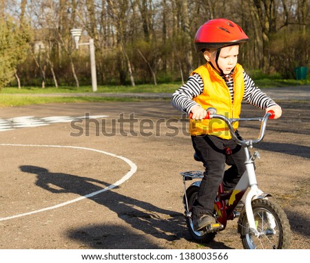 Cute little boy dressed in a safety helmet and high visibility jacket pedalling his bike on a quiet country road
