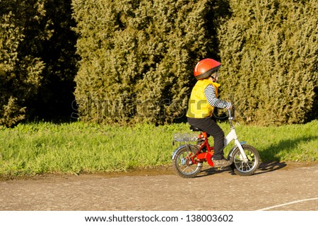 Active little boy dressed in a colourful safety helmet and high visibility jacket out riding his bike on a quiet lane past a row of cypress trees