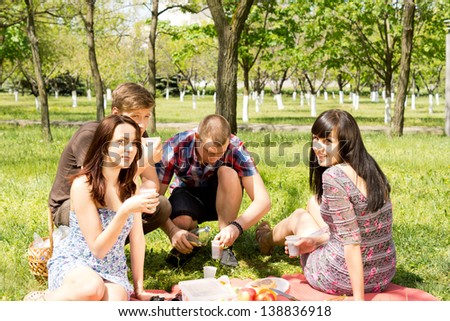 Two attractive young couples enjoying a picnic on lush green grass in a wooded park