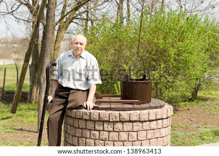 One legged man sitting on an old well in a rural park looking at the camera holding his crutches in one hand