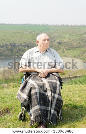 Happy disabled senior man enjoying the sun sitting on a hilltop with scenic views with a blanket over his legs
