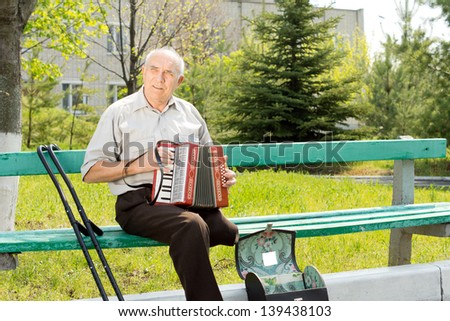 Disabled senior man with one leg amputated above the knee sitting on a park bench playing the accordion