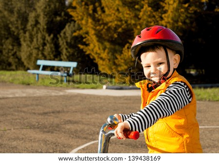 Happy small boy out riding his bicycle wearing a safety helmet and orange high visibility jacket giving the camera a lovely smile as he enjoys himself on a quiet country lane