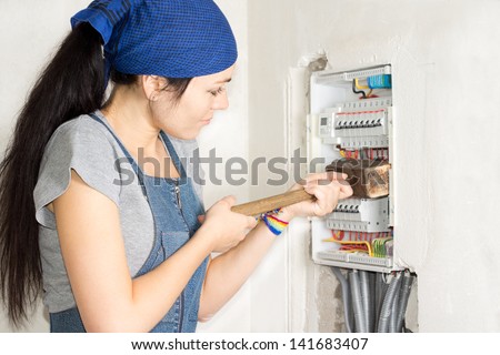 Housewife armed with a wooden mallet attacking an open electrical fuse box in frustration as she tries to solve her problems