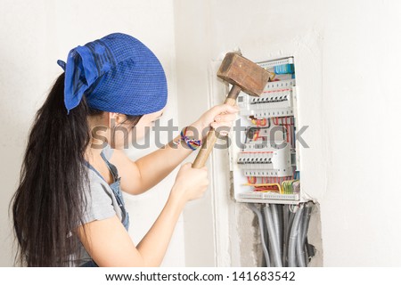 Woman taking aim at an electrical fuse box with a large wooden mallet in an effort to solve her supply problems