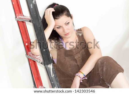Tired woman sitting at the foot of a stepladder with her head on her hands as she takes a break from renovating her house