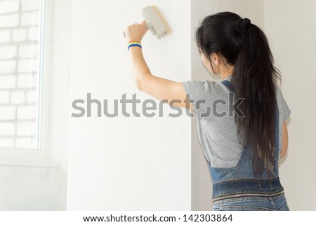 Rear view woman paints the wall roller of her new apartment