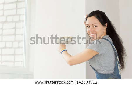 Smiling woman standing looking at the camera painting a section of wall during a renovation project