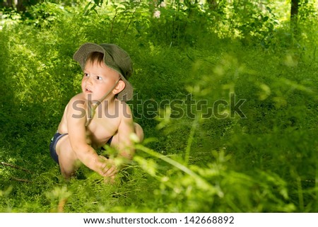 Surprised young small boy discovering nature, while crouching and playing with wild plants in the woods