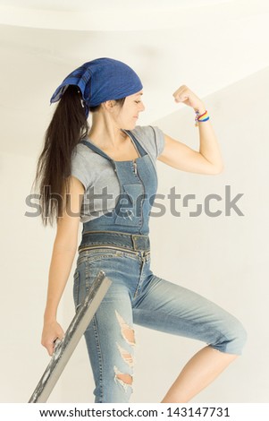 Beautiful female carpenter shows her muscle and holding paint scraper