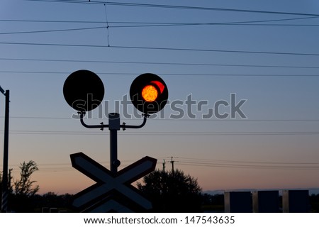 Railroad red traffic signal at a level crossing or grade crossing warning cars of an approaching train at dusk