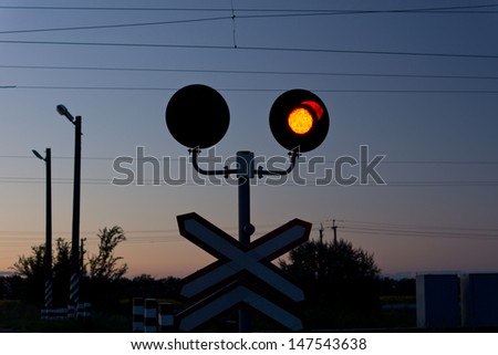 Red signal at a railway crossing above a traffic sign as a warning to cars to stop and not cross the lines as there is an approaching train