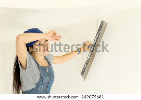 Hardworking woman holds a paint scraper working on wall