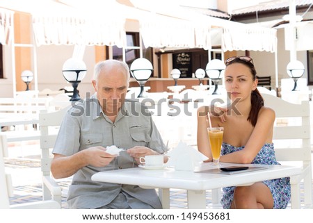 An elderly father and his attractive daughter having coffee together at an outdoor restaurant on a hot summer day