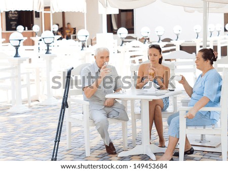 Family enjoying a drink together with elderly parents and their daughter sitting at an open-air restaurant, the man is an amputee on crutches