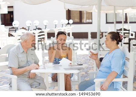 Elderly parents lunching with their daughter sitting together in the shade of an umbrella at an outdoor restaurant in summer