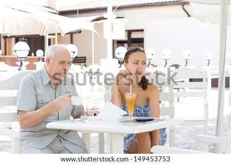 Couple having drinks at an outdoor cafe with an elderly man and attractive younger woman sitting at a table in the shade of an umbrella