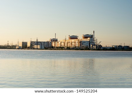 View across the water of an industrial building, refinery, factory, plant or mill on the edge of a waterway with storage tanks and electricity pylons