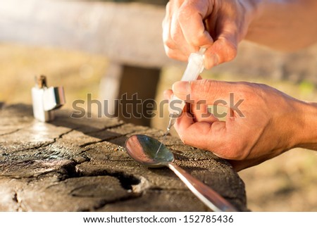 Close-up of male hands filling a syringe with soluble drug from a silver spoon