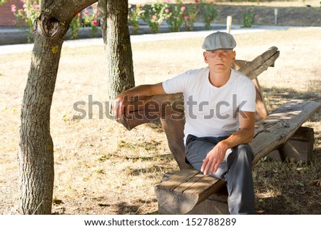 Solitary Caucasian middle-aged man thinking while sitting on a bench in the park in a warm day of summer