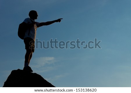 Silhouette of a man standing on the mountain top and pointing straight ahead to an unknown destination