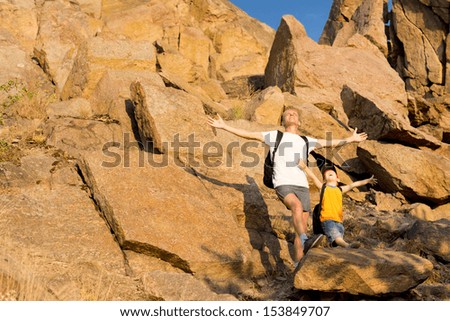 Father and his small son on a rocky mountain standing on a ledge with their arms open wide to the summer sunshine as they celebrate nature
