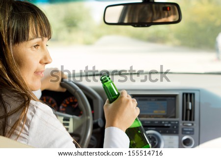 Drunk female driver drinking alcohol from the bottle turning and talking to a passenger while driving down a road losing all concentration