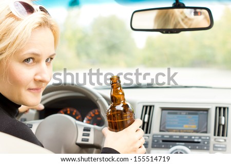 Smiling female driver drinking alcohol from a bottle and turning to the passenger side and talking, completely losing all concentration on the road