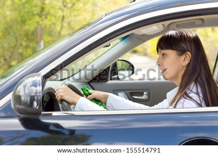Drunk female driver with impaired ability staring blearily at her dashboard while gripping the wheel tightly and holding onto her bottle of alcohol