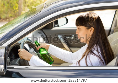 Dangerous driving with a drunk and inebriated female driver staring blearily at her steering wheel as she drives along holding a bottle of booze in her hand