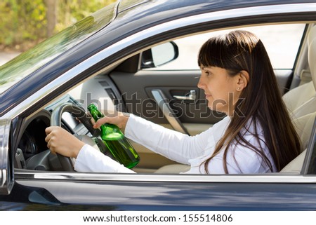 Drunk woman driver smiling as she drives with a bottle of alcohol clutched tightly in one hand, view through the side window