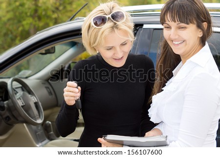 Clinching the deal as the new attractive blond female owner of a car stands ready to sign the contract with the smiling saleswoman