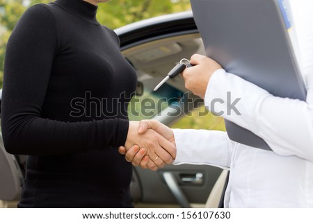Two women shaking hands to finalise the deal on the sale of a new car with the saleslady holding the contract and keys in her hand