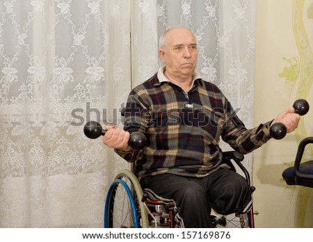 Senior handicapped male amputee sitting in his wheelchair doing exercises working out with a pair of dumbbells
