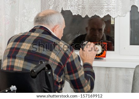 Handicapped man in a wheelchair sitting with a clock in front of him waiting patiently at a window at night for someone to arrive