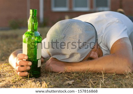 Drunk Caucasian man sleeping on the ground holding a bottle of white wine