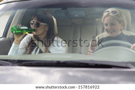 Two attractive women partying and drinking while driving along in a car, view through the front windscreen