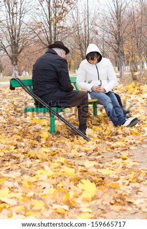 Disabled elderly man with crutches and an attractive younger woman playing chess sitting together on a wooden park bench wrapped up warmly against the cold autumn weather