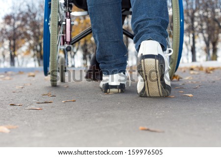 Low angle view of the feet of a person in jeans and sneakers pushing a wheelchair down the street