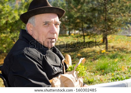 Elderly gentleman in a wheelchair with his groceries in a brown paper packet on his lap as he returns from the shops, close up portrait