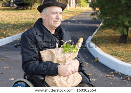 Smiling elderly gentleman sitting in a wheelchair in the road with his brown paper bag of groceries clutched in his arms